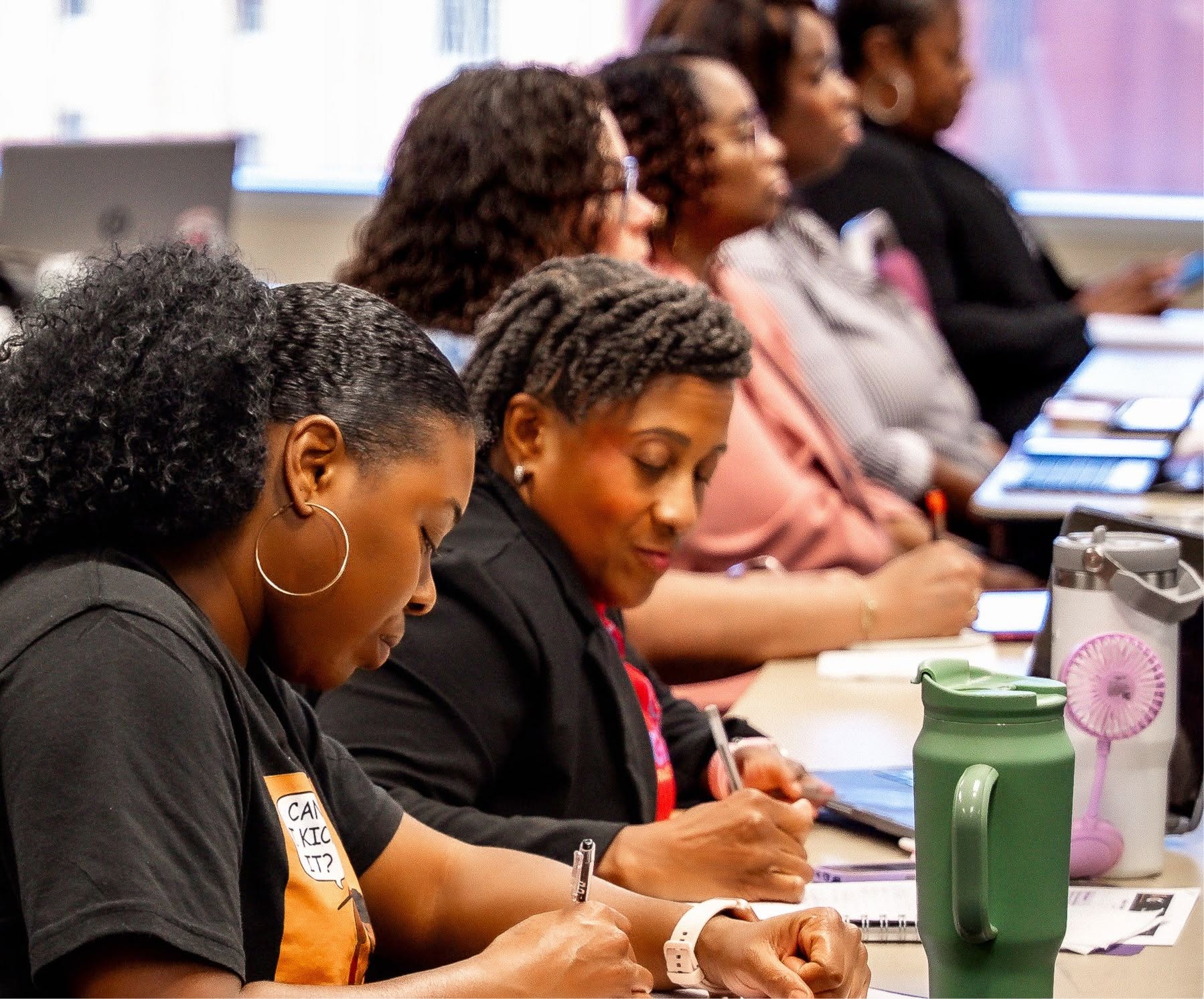Two B.I.D. Academy participants taking handwritten notes side by side during a session.